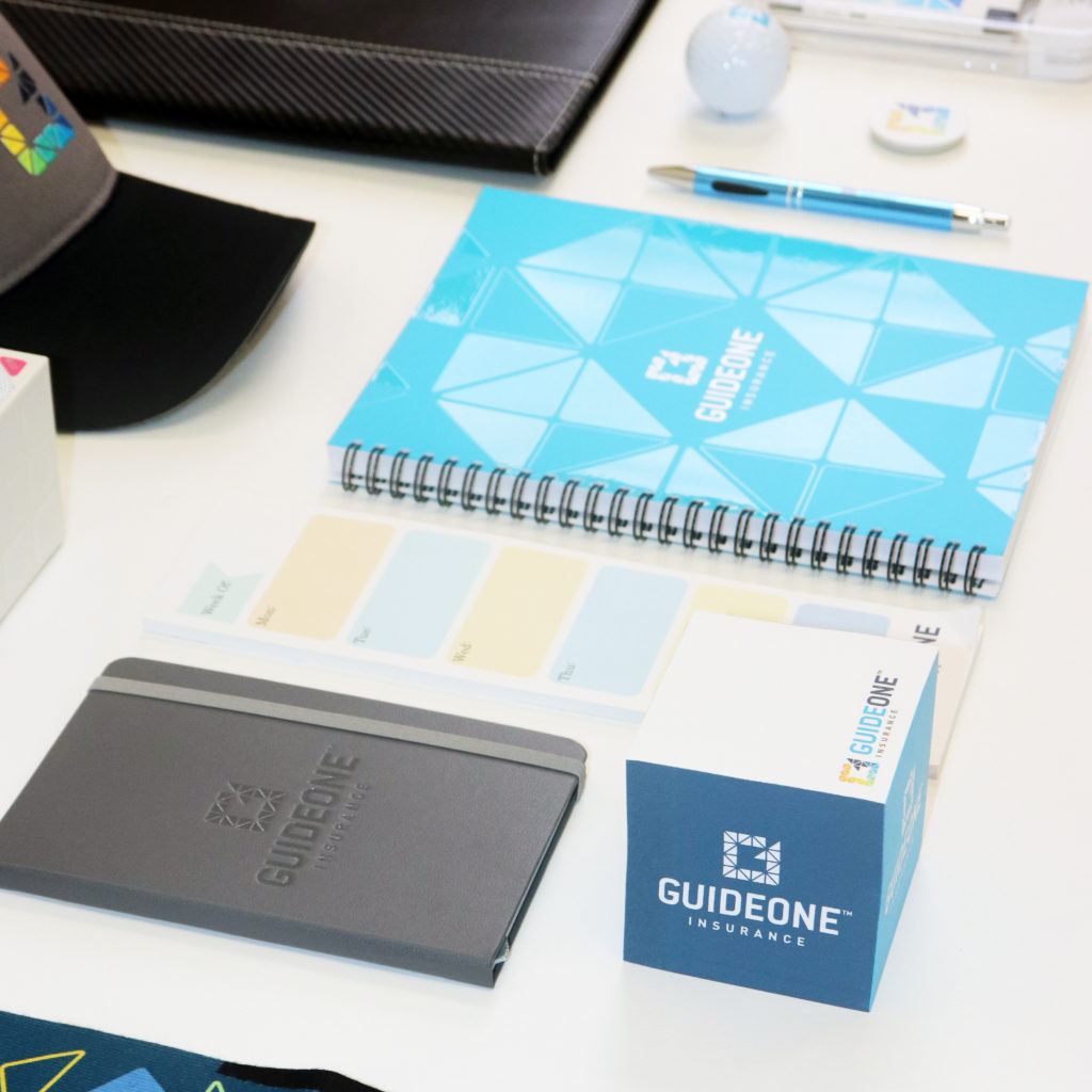 Guideone Insurance promotional items including: hats, padfolio, ball, tumbler, pen, notebook, post its